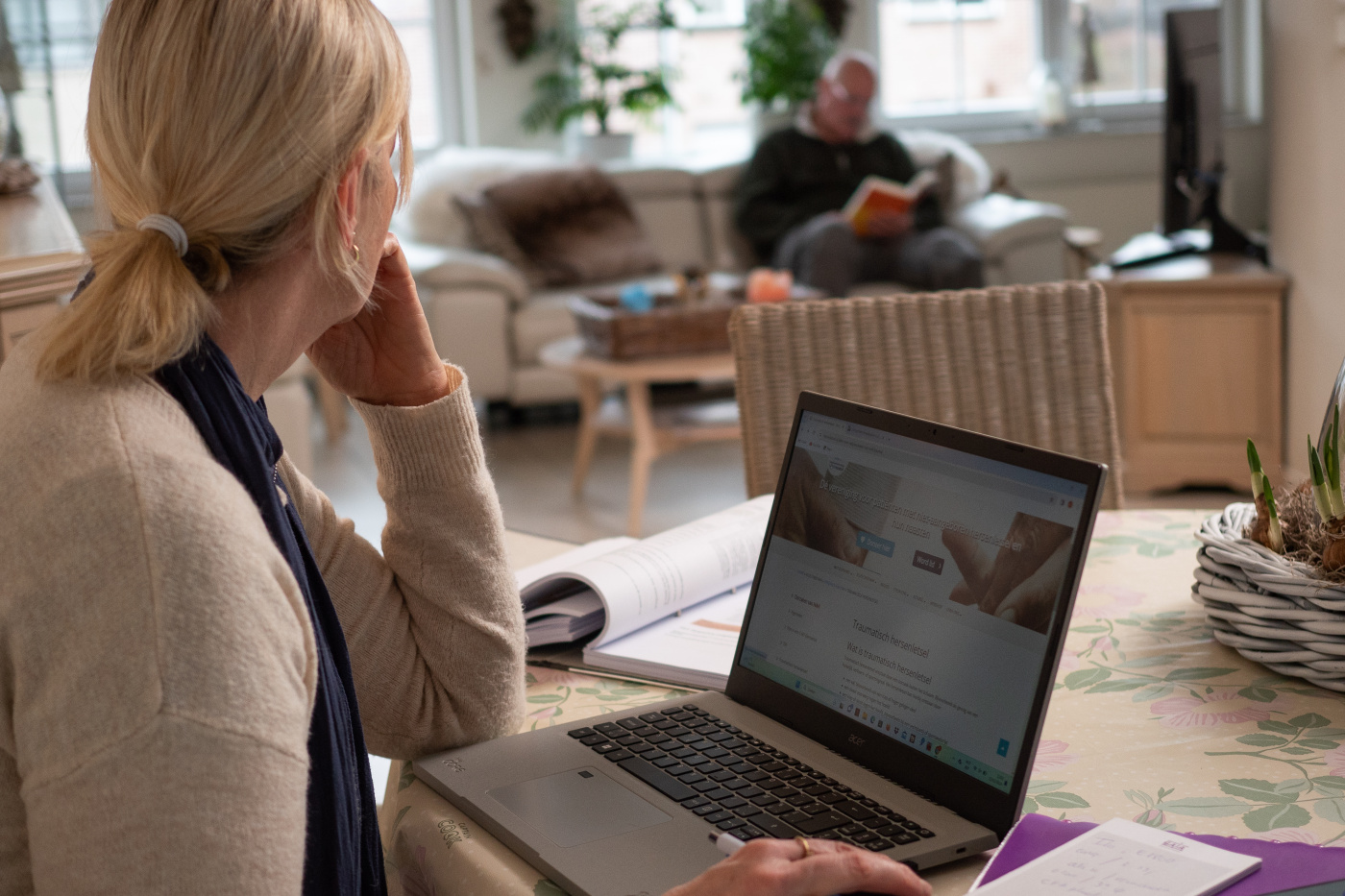 Brigitte werkt op haar laptop terwijl haar echtgenoot in de zetel zit